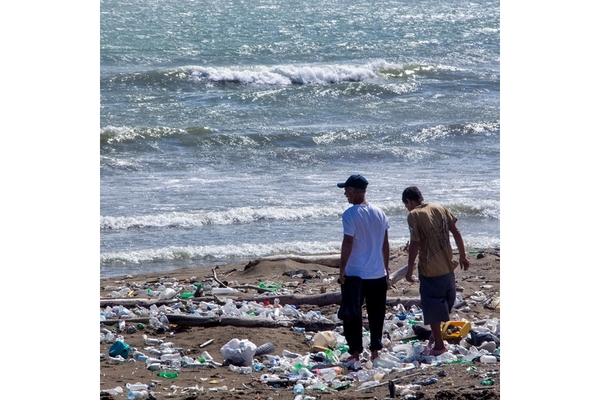 Two men on a beach surrounded by litter and plastic bottles, highlighting the issue of pollution.